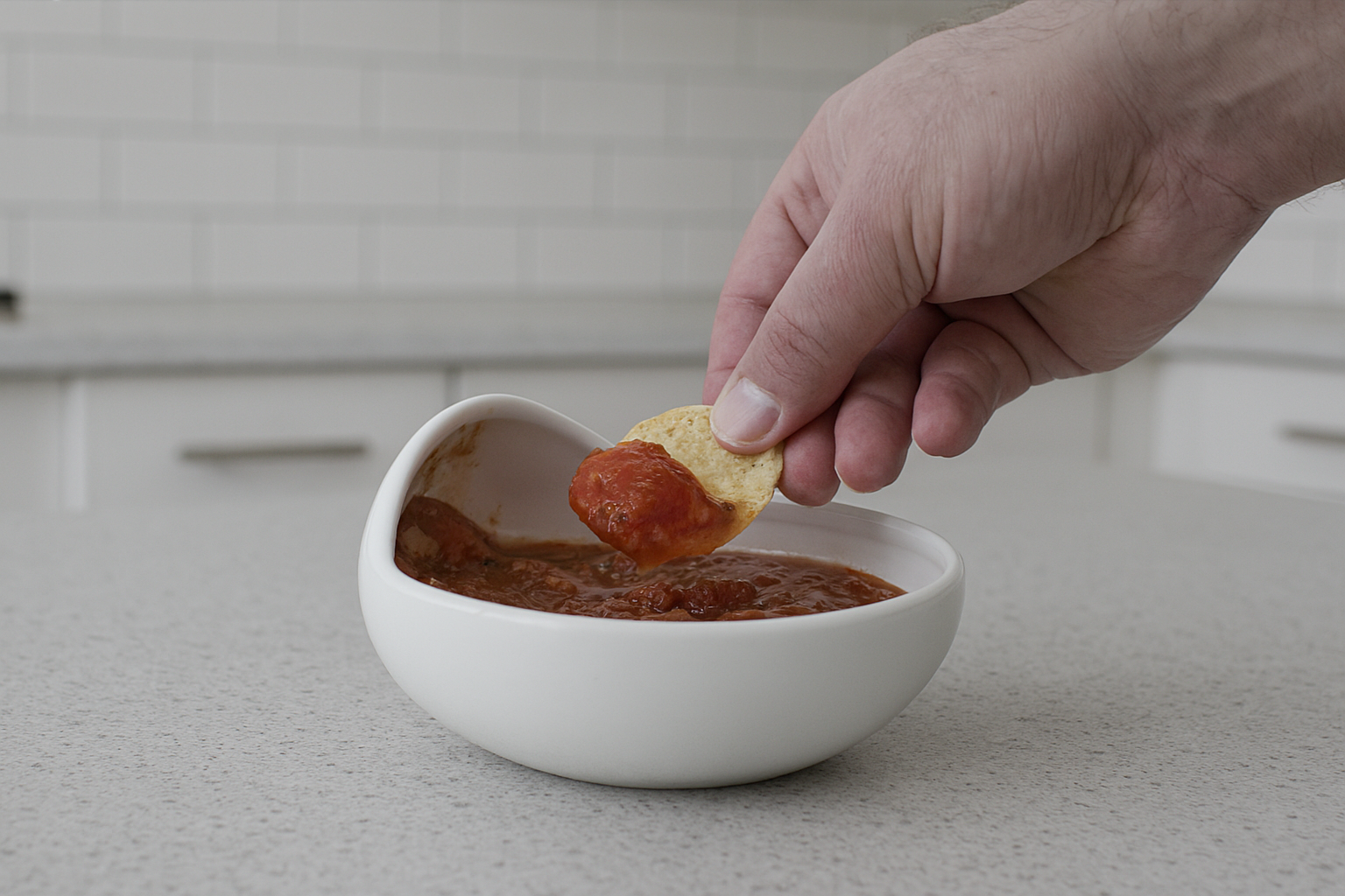 Hand dipping chip with salsa in The Palada bowl