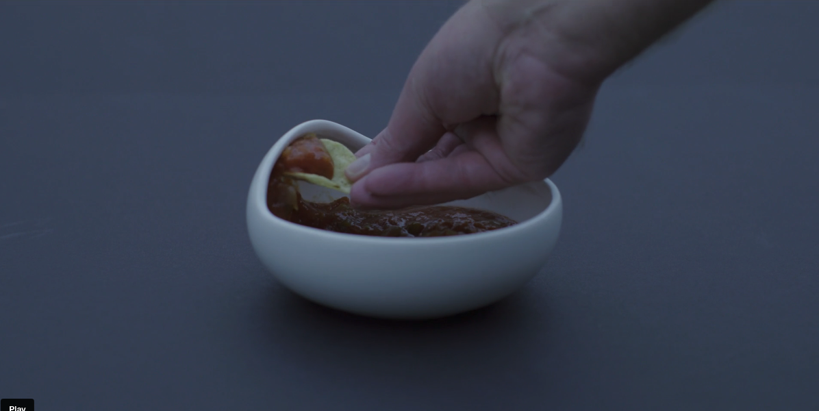 Hand dipping chip into The Palada bowl showing the non-spill ridge in action